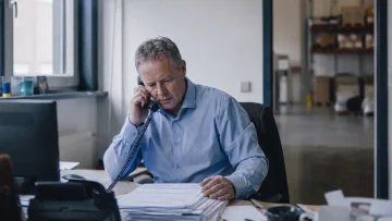 Ondernemer aan de telefoon achter een bureau met een stapel facturen